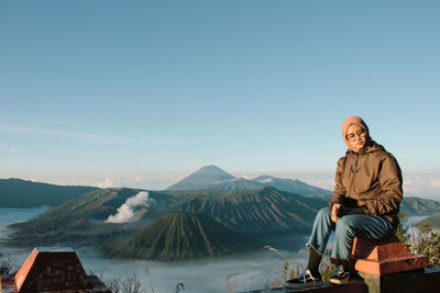 Full length of man sitting on mountain against sky