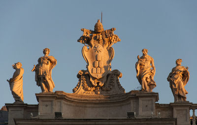 Low angle view of statues on building against clear blue sky