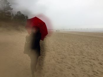 Man with umbrella on beach against sky