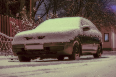 Snow covered car on street against trees in city