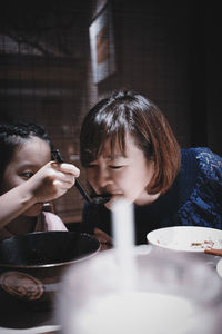 Daughter feeding mother food while sitting in restaurant