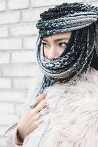 Beautiful woman with braided hair standing against wall