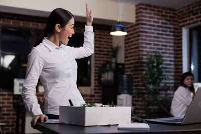 Happy businesswoman with hand raised at office