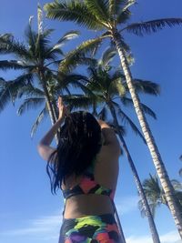 Low angle view of woman standing by palm tree against sky