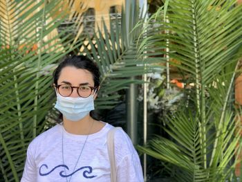 Portrait of young woman wearing mask standing against plants