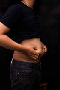 Midsection of man holding stomach while standing against black background