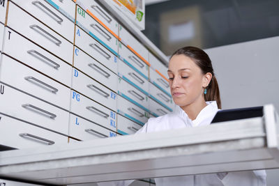 Low angle view of woman wearing lab coat while sitting by cabinet