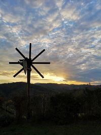 Silhouette cross on field against sky during sunset