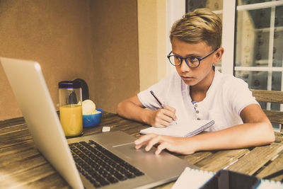 Cute boy using laptop while studying on table at home