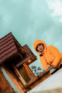 Low angle portrait of man standing on roof against sky