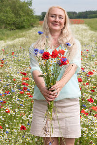 Beautiful middle-aged blonde woman stands among a flowering field of poppies