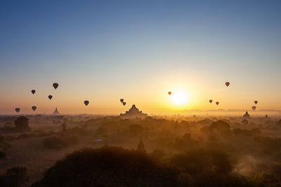 Silhouette hot air balloons flying over landscape against sky during sunset