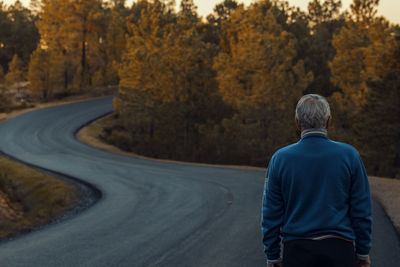 Rear view of senior man on road amidst trees during autumn