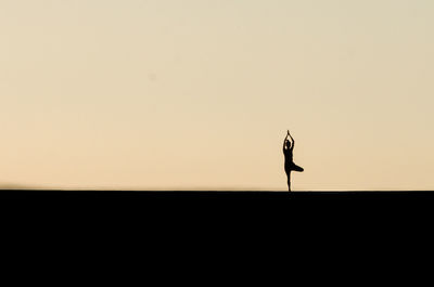 Silhouette woman in tree pose on field against clear sky during sunset