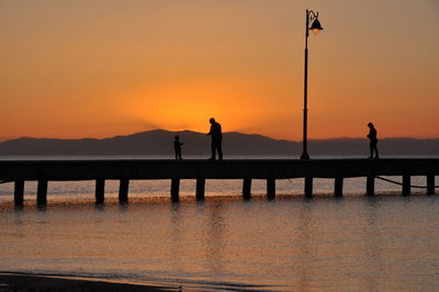 Silhouette people on pier in river against sky during sunset