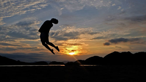 Silhouette of woman jumping at sunset