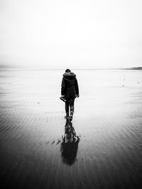 Rear view of man walking on wet beach
