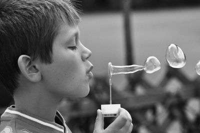 Side view of boy blowing bubbles outdoors