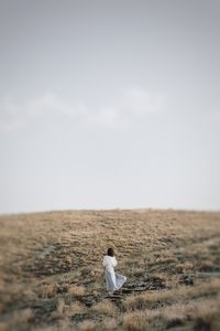 Rear view of man sitting on field against sky