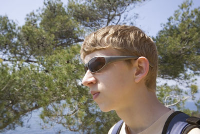 Low angle view of teenage boy wearing sunglasses standing against trees