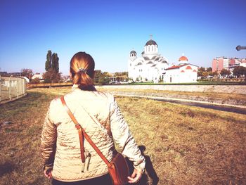 Rear view of woman walking by building against sky