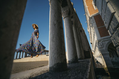 Low angle view of woman on bridge seen through railings in city