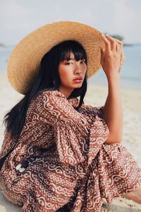 Portrait of young woman wearing hat sitting at beach