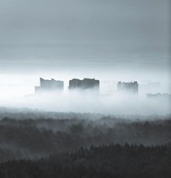 Scenic view of foggy forest and buildings against sky
