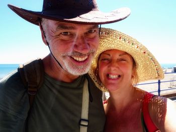 Portrait of smiling mature couple wearing hats at beach during summer