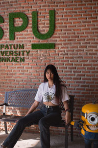 Portrait of young woman sitting on chair against brick wall