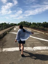 Rear view of man walking on road against sky