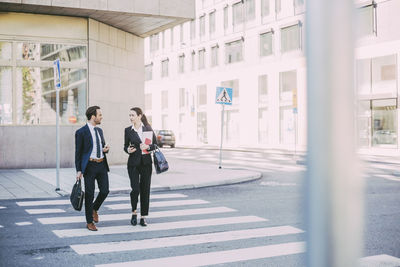 Full length of business coworkers talking wile crossing road in city