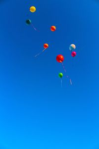 Low angle view of balloons flying against clear blue sky