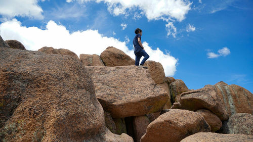 Low angle view of man standing on rock against sky