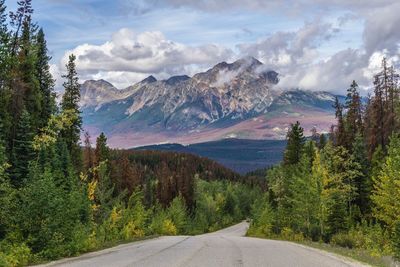 Road amidst trees and mountains against sky