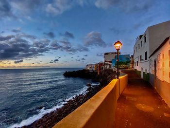 Scenic view of beach by buildings against sky during sunset