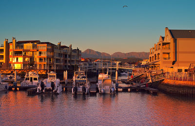 Buildings by river against clear sky during sunset