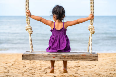 Rear view of girl sitting on swing at beach