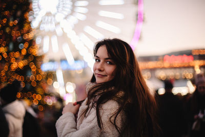 Portrait of young woman standing in christmas market in the evening