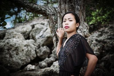 Portrait of woman on rock against tree trunk