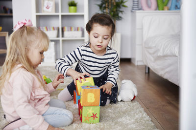 Two little girls playing with toy blocks on carpet at home