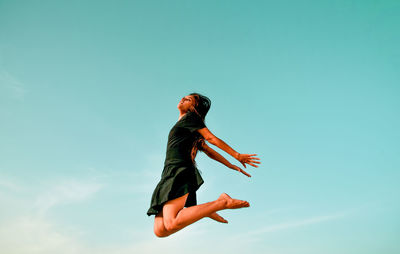 Low angle view of woman jumping against clear blue sky