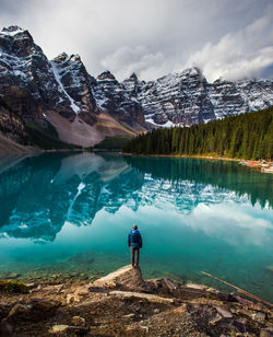 Woman looking at lake by snowcapped mountain against sky