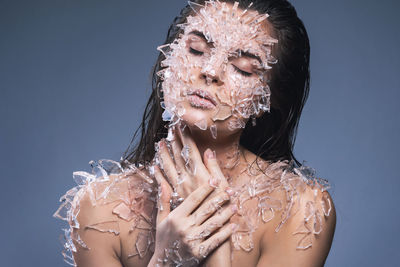 Close-up of woman with broken glass on body against purple background