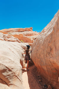 Low angle view of man standing on rock formations against clear blue sky