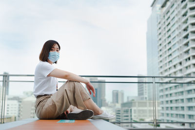 Solo asian woman wear protective mask during outdoor break and relax at rooftop with city background