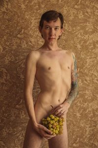 Portrait of a shirtless man standing against a wall with grapes