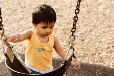 Cute baby boy standing by swing at playground