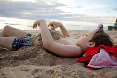 Rear view of girl lying on sand at beach against sky