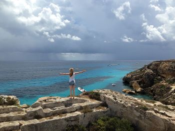 Rear view of woman standing with arms outstretched on rock formation while looking at horizon